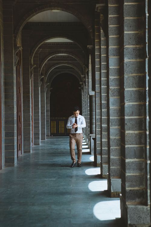 Free A man in a dress shirt and pants walks through a historic colonnade corridor, creating an urban and architectural scene. Stock Photo