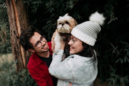 Woman Lifting Puppy in Front of Man Near Tree