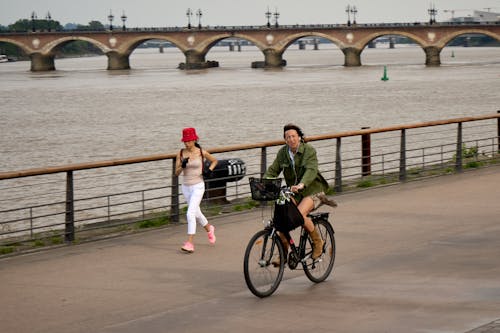Bordeaux, France, 05.23.2023 A cycling woman in trendy attire blends harmoniously with urban life. Pont de Pierre (Stone Bridge) stretches over the tranquil water of the river Garonne.