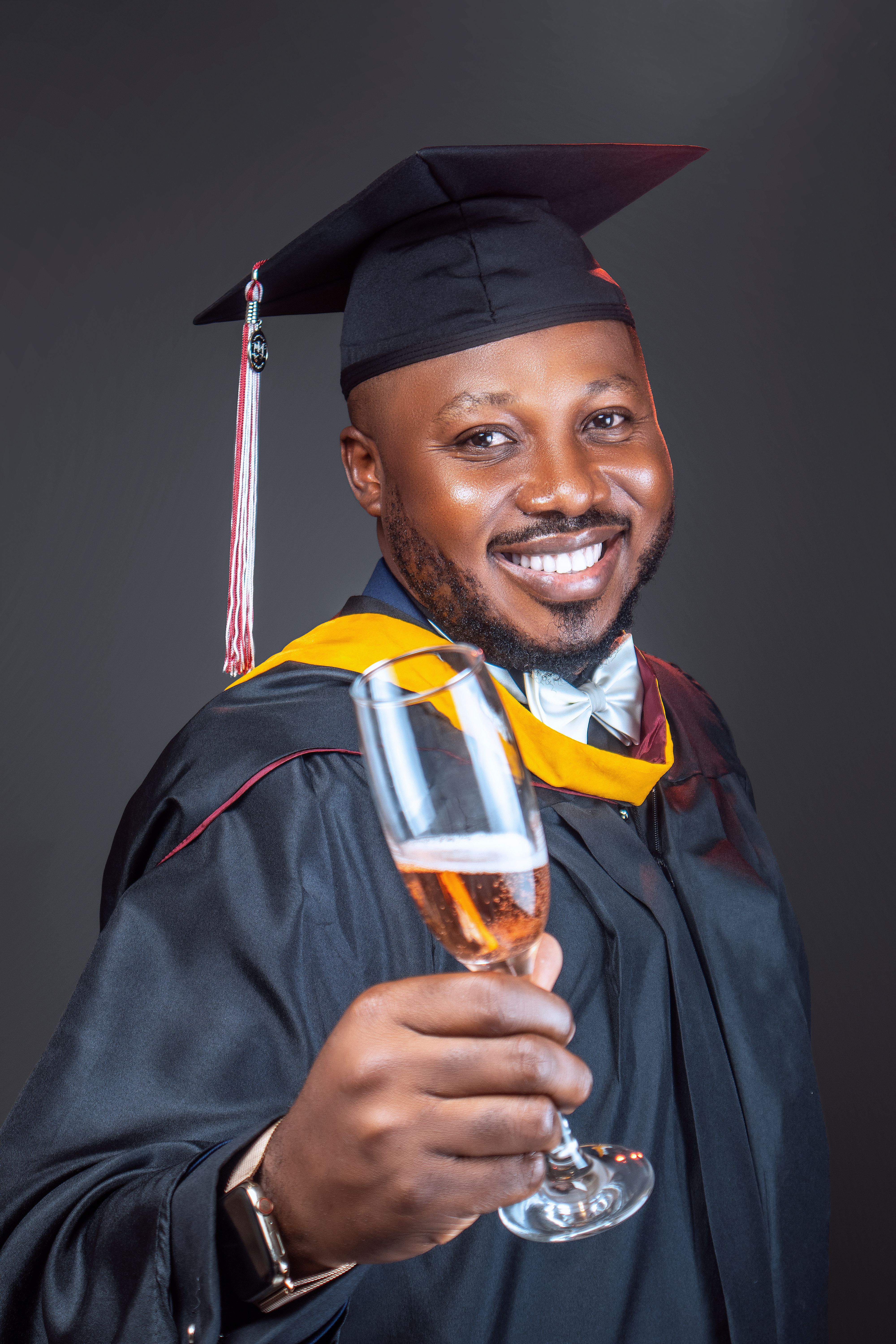 A proud graduate celebrates with a toast, smiling in cap and gown.