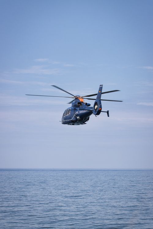 Free A helicopter glides gracefully above a serene open sea under a clear blue sky. Stock Photo