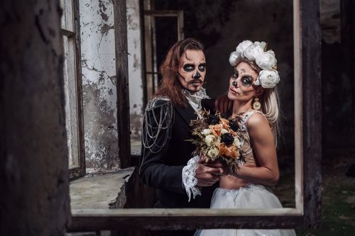 Free Couple dressed in Day of the Dead makeup and costumes holding flowers indoors. Stock Photo