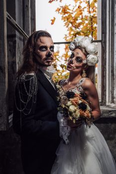 Halloween-themed wedding couple with skull makeup and autumn backdrop.