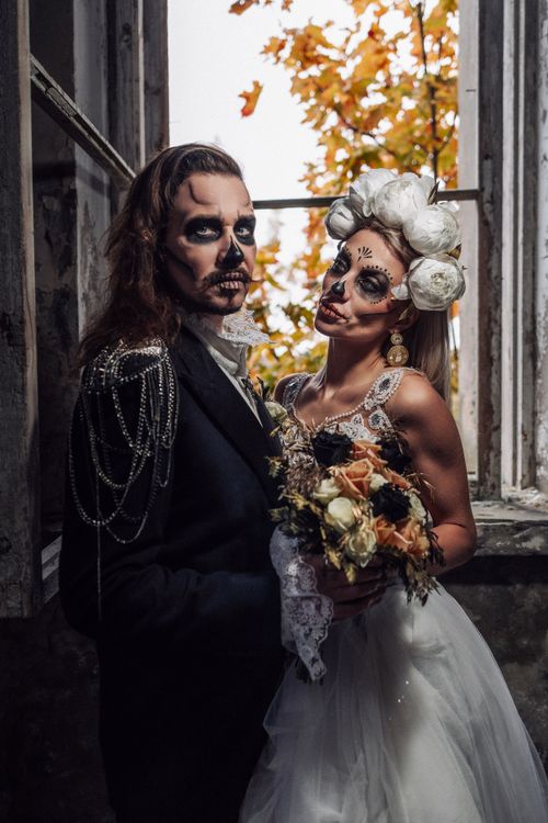 Free Halloween-themed wedding couple with skull makeup and autumn backdrop. Stock Photo