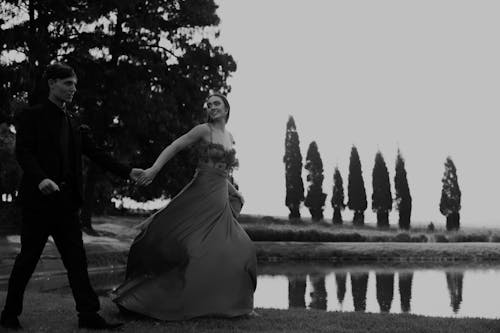 Black and White Photo of a Couple in Elegant Clothes Walking in a Park 