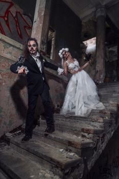 A spooky bride and groom pose in a haunted, abandoned setting with dramatic makeup.
