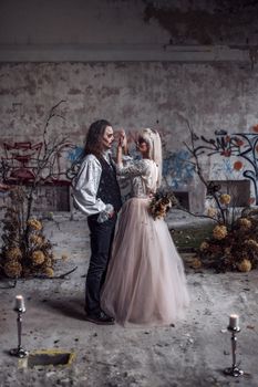 A couple poses in Halloween-themed costumes in an abandoned venue decorated for a wedding.