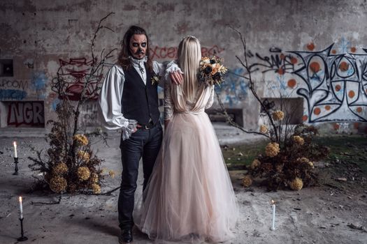 A couple in Halloween costumes poses in an abandoned graffiti-covered building.