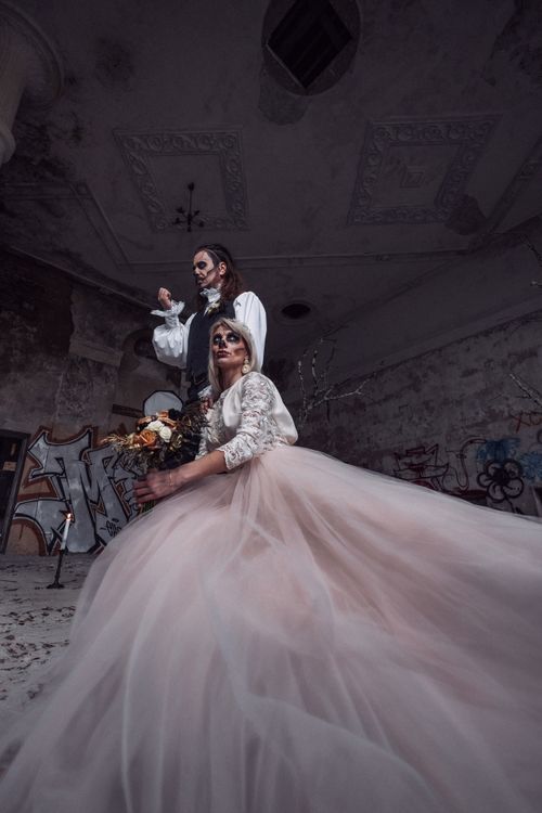 Free A bride and groom in Halloween costumes pose in an abandoned, graffiti-covered building. Stock Photo