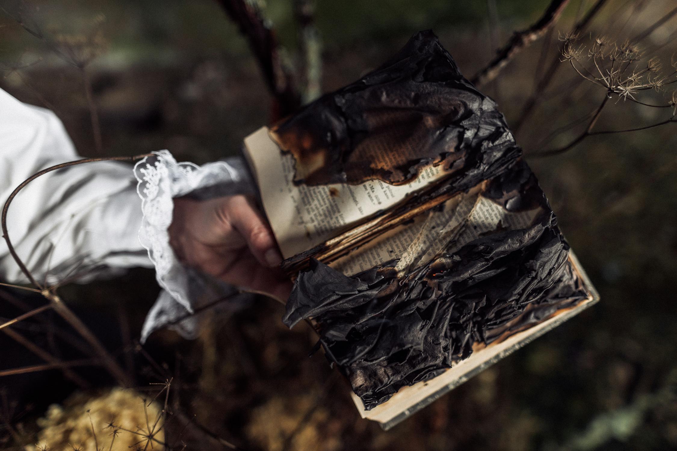 Un livre partiellement brûlé tenu par une main vêtue d'une manche en dentelle.