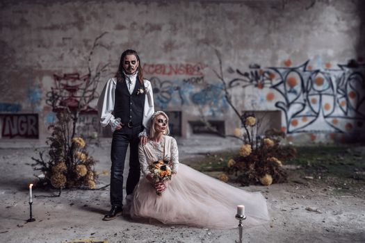 A couple with gothic Halloween makeup poses in an abandoned graffiti-covered building.
