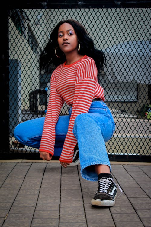 Photo of Woman in Red and White Striped Long-sleeved Shirt and Blue Jeans Squat Posing