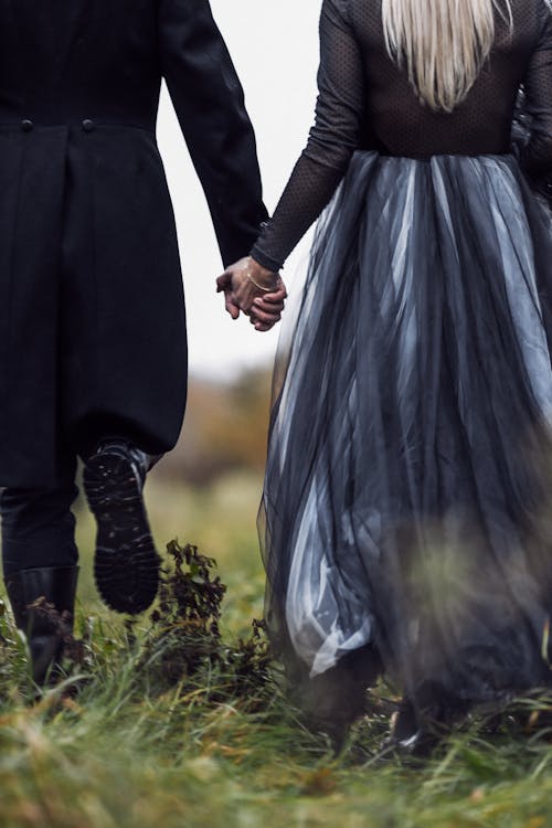 Back View of a Couple Walking on a Meadow and Holding Hands 