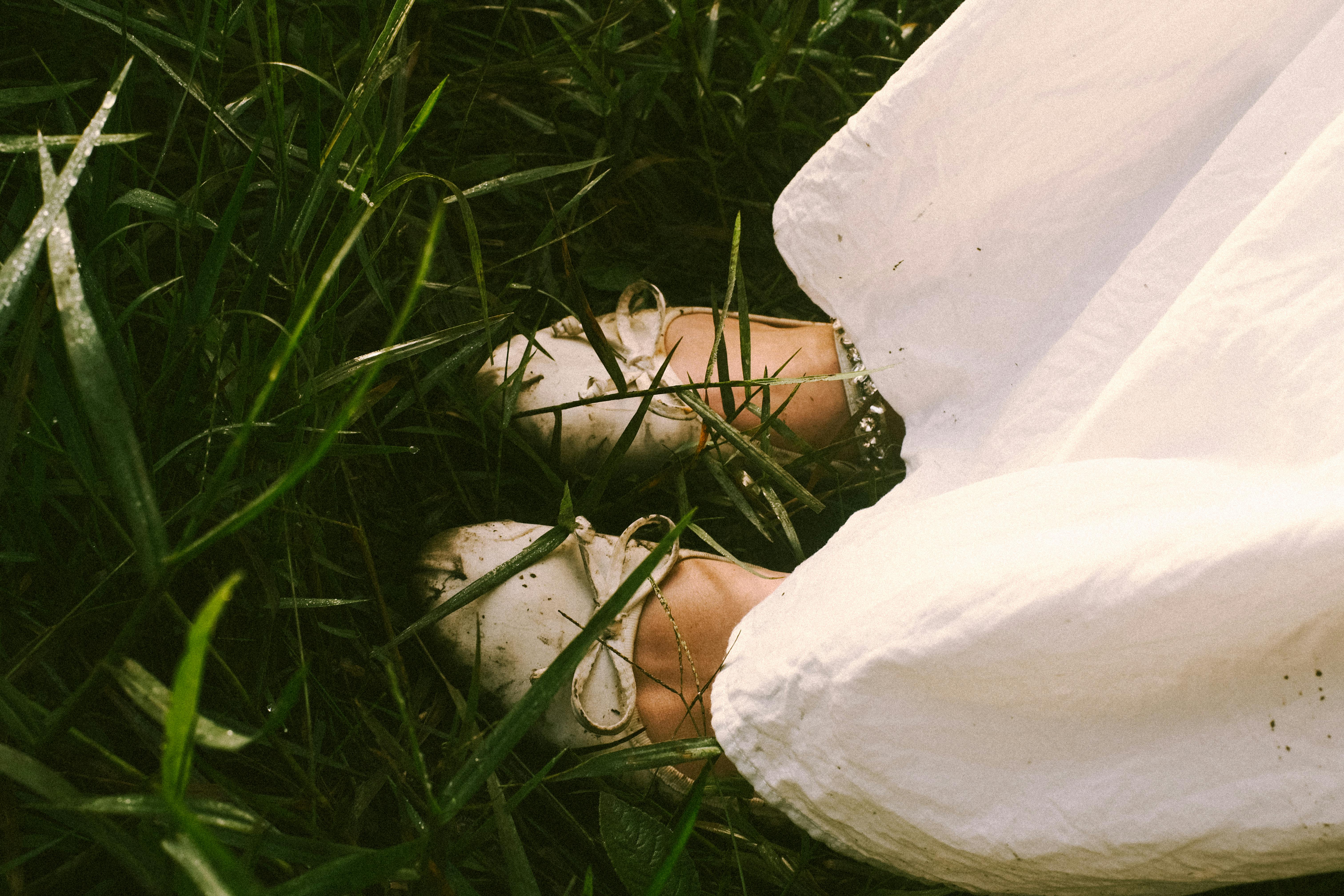 Close-up of white shoes and dress in lush grass, capturing a serene outdoor moment.