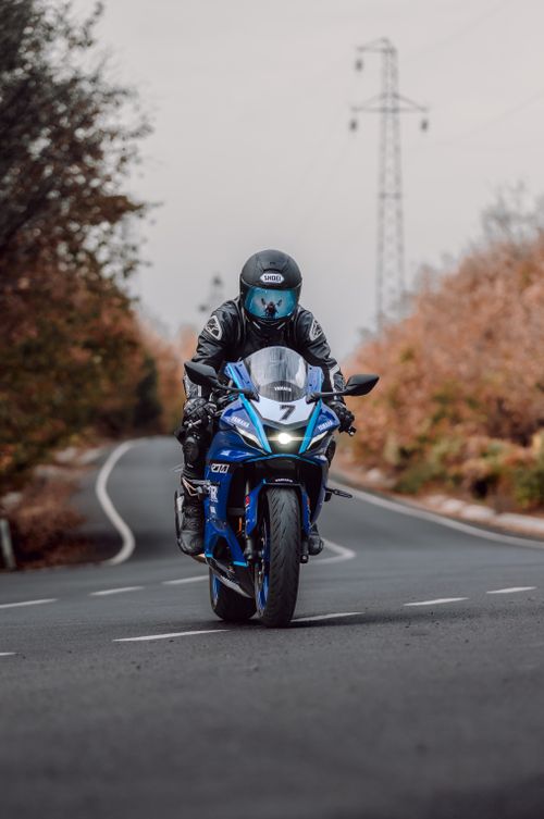 Free Motorcyclist in full gear riding a blue motorcycle down a quiet, tree-lined road during fall. Stock Photo