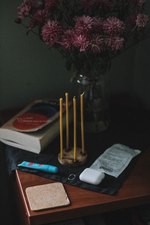 Free Moody still life featuring flowers, a book, candles, and personal items on a wooden table. Stock Photo