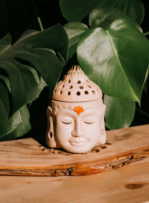 Free Peaceful Buddha head candle holder surrounded by lush green leaves on a wooden surface. Stock Photo