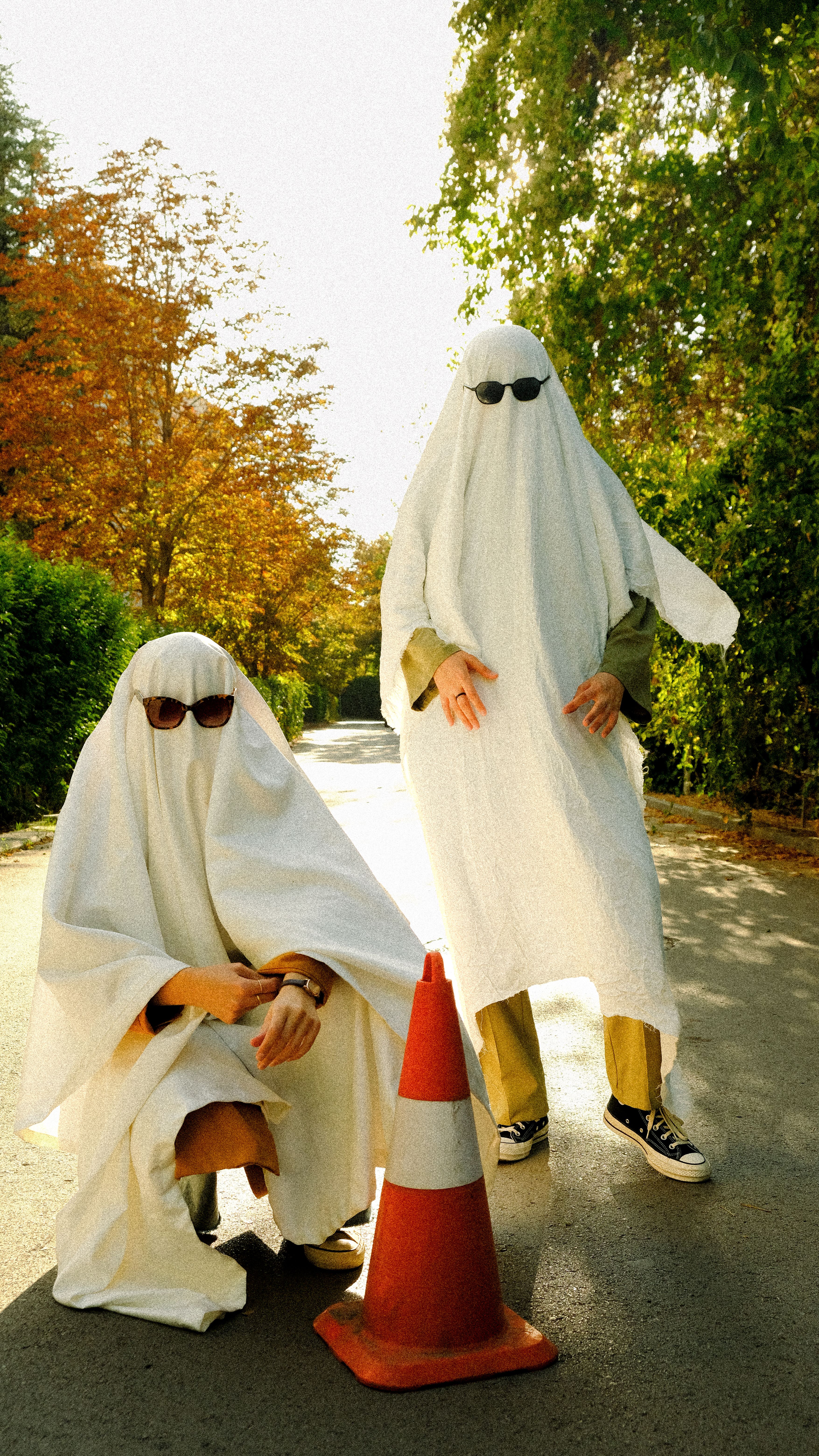 People in ghost costumes with sunglasses enjoy a sunny autumn day outdoors.