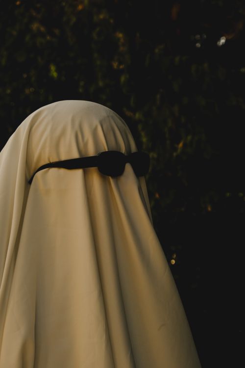 Free A ghostly figure draped in white fabric wearing sunglasses, perfect for a playful Halloween theme. Stock Photo