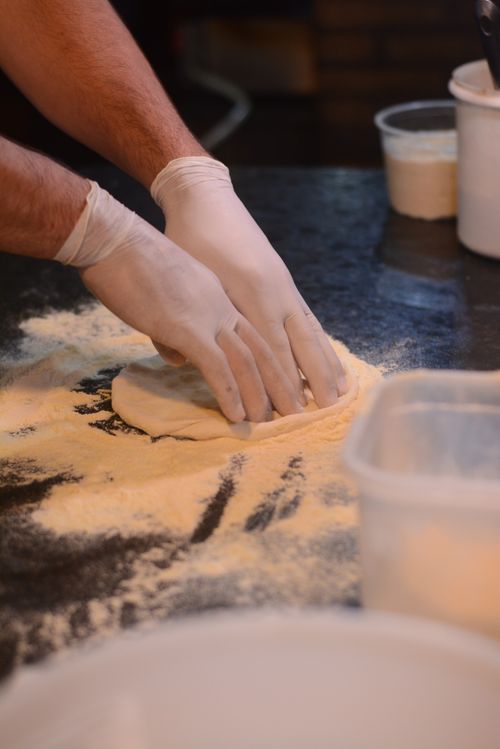 Free Chef wearing gloves prepares pizza dough with flour in a kitchen setting. Stock Photo