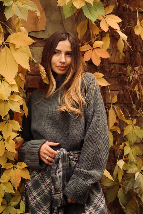 Model with a Plaid Shirt Tied Over a Gray Sweater Standing in Front of a Brick Wall Overgrown by Vines