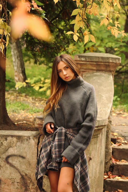 Model in a Gray Sweater and a Plaid Shirt Tied Around Her Waist Posing in a Park