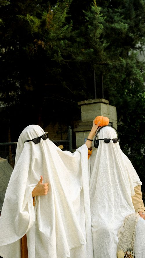Free Two people in ghost costumes with sunglasses, holding a pumpkin outdoors. Stock Photo