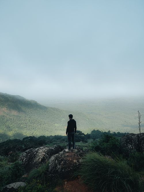 Free A man stands on a rocky cliff, gazing at a vast, fog-covered landscape below. Stock Photo