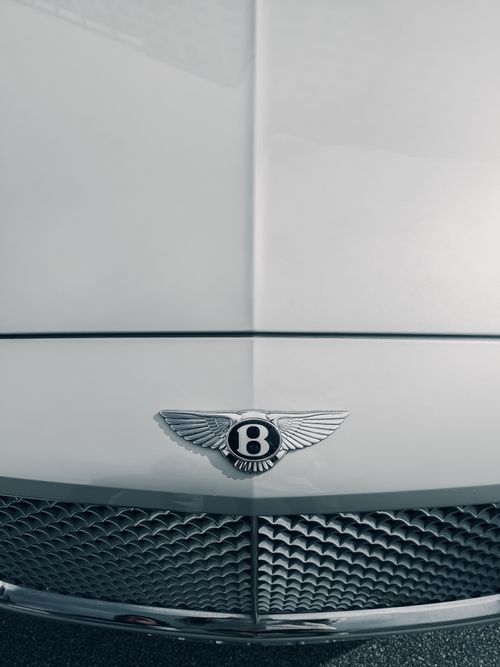 Free Close-up of a Bentley car emblem on a white vehicle, showcasing elegance and luxury. Stock Photo