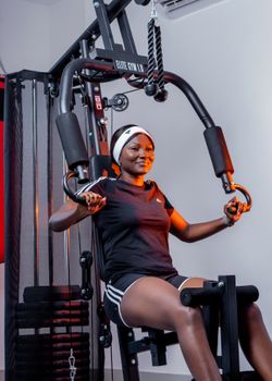 Young African woman working out on exercise machine indoors, promoting fitness and health