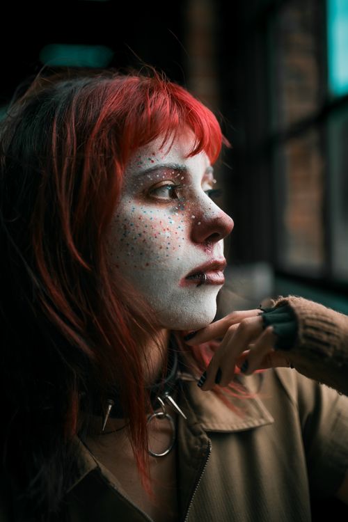 Free Close-up of a woman with red hair and painted face, looking thoughtfully out of a window. Stock Photo