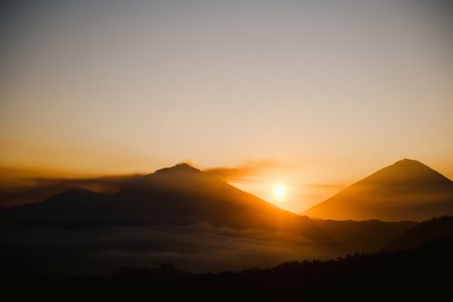 Free A tranquil sunrise scene with misty mountains and a warm glow in the sky. Stock Photo