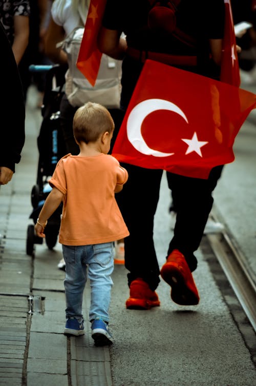 Back View of a Little Boy and a Person with Turkish Flag Walking on the Sidewalk 