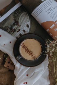 Top view of a coffee cup on a black saucer with an open magazine, creating a cozy still life scene.