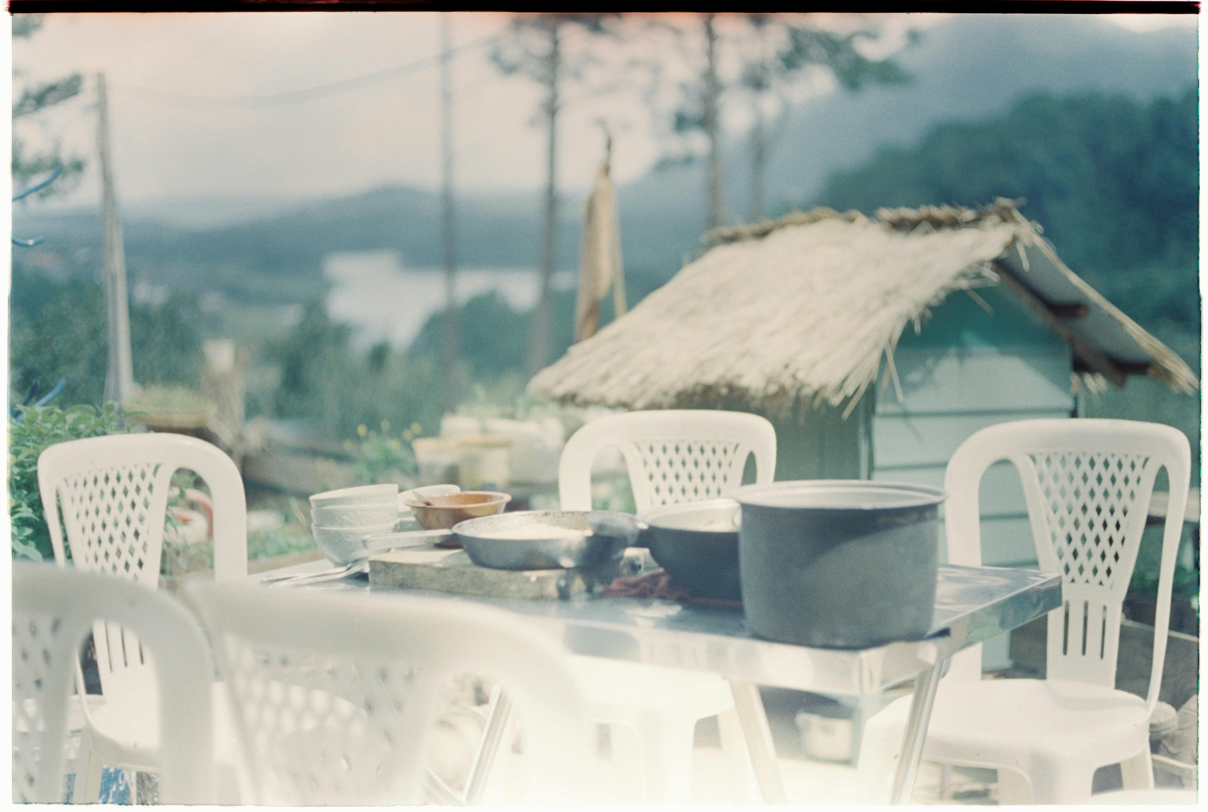 An outdoor dining area with plastic chairs and kitchenware in a lush, tropical setting.