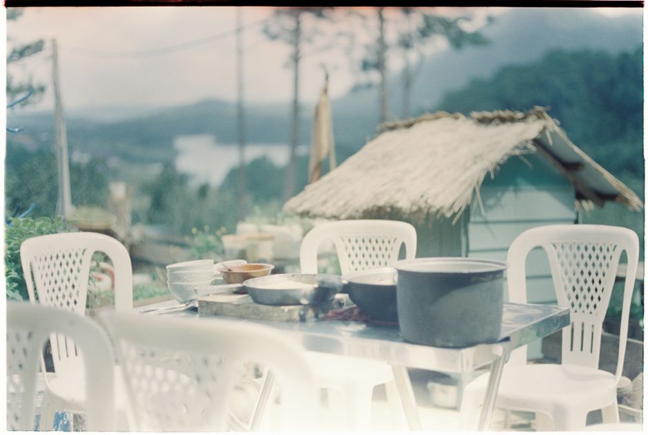 An outdoor dining area with plastic chairs and kitchenware in a lush, tropical setting.