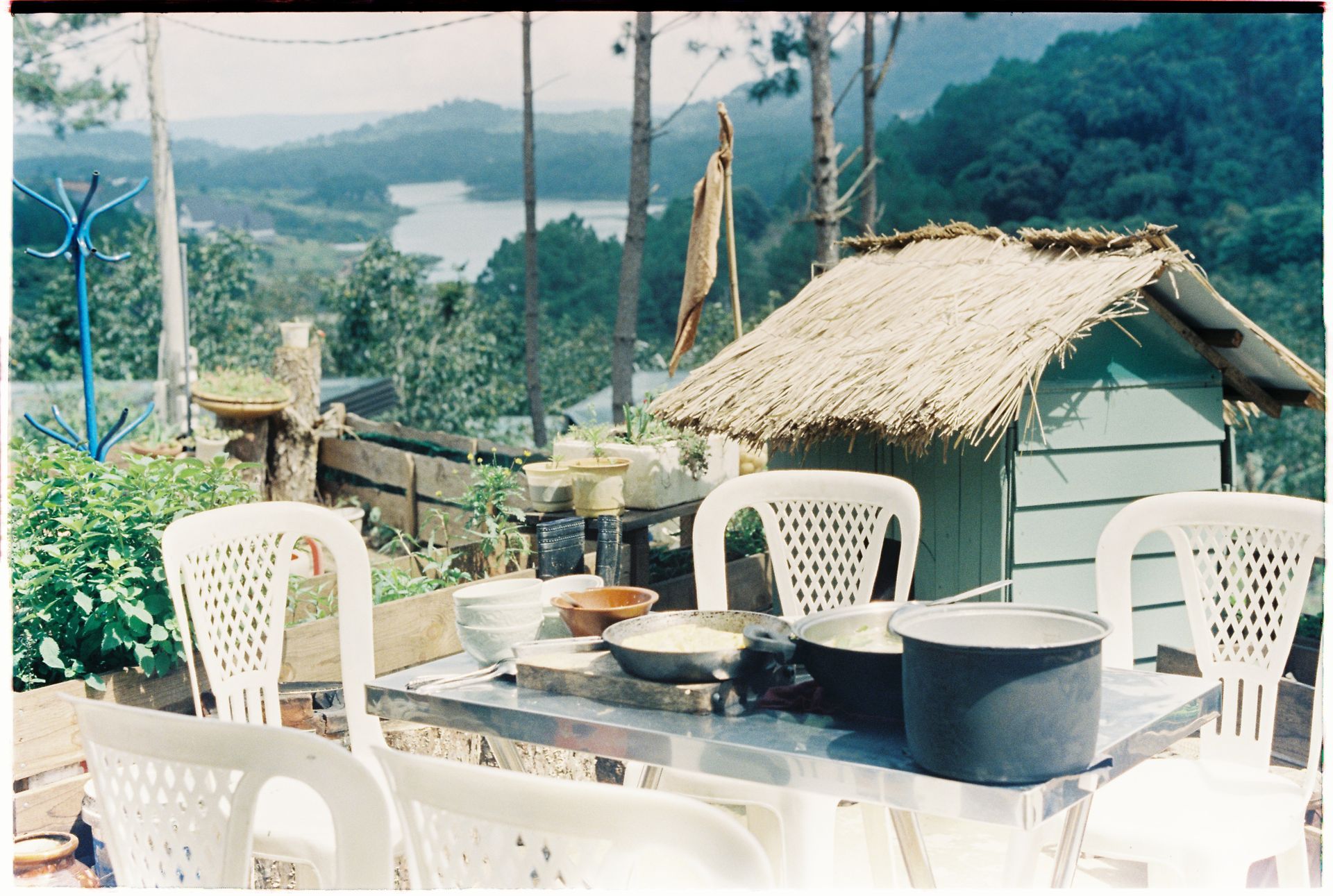 Outdoor terrace dining with plastic chairs and a scenic view of lush hills and a lake.