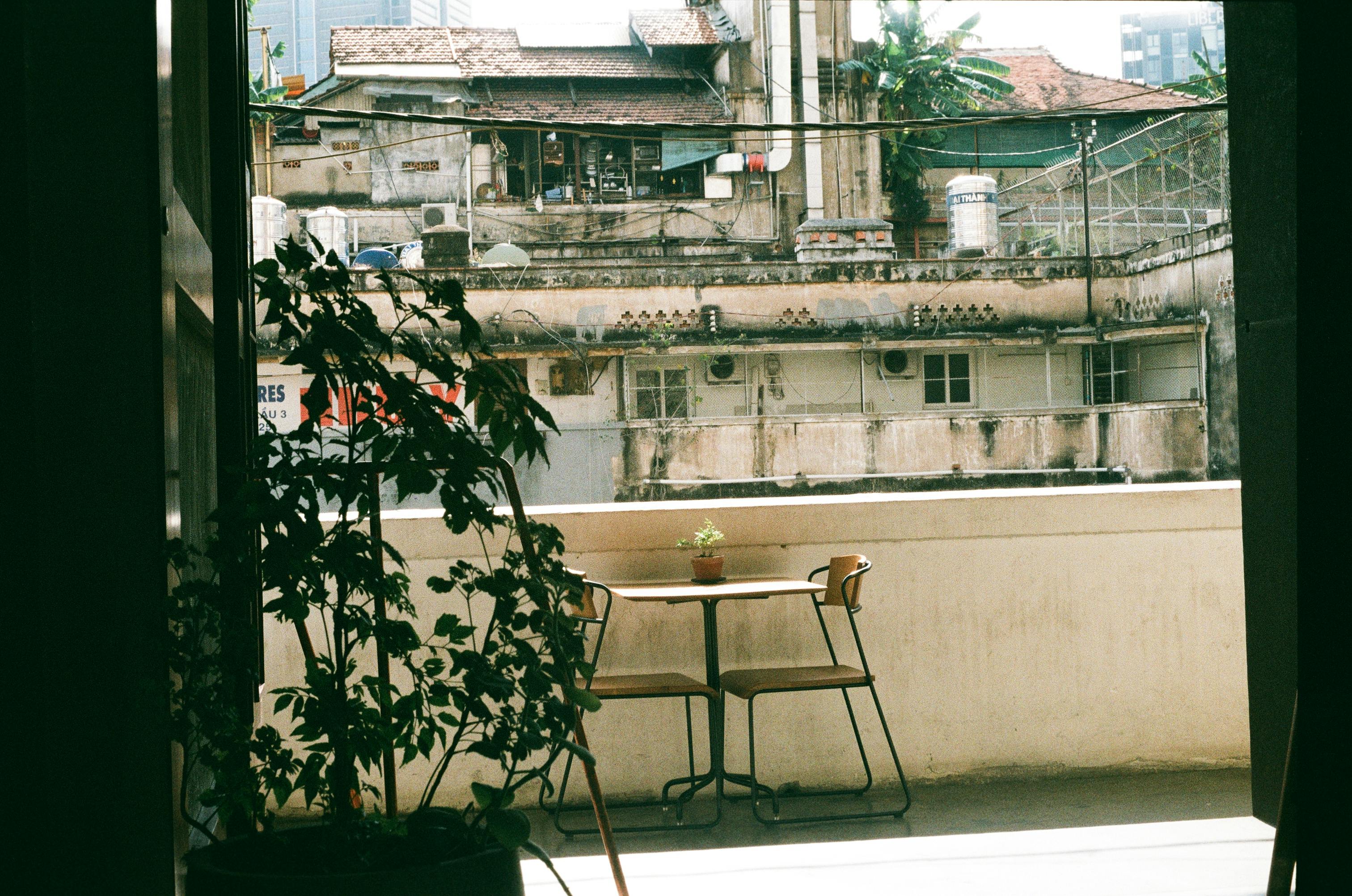 A peaceful balcony in an urban setting featuring a table, chairs, and potted plant with rustic views.