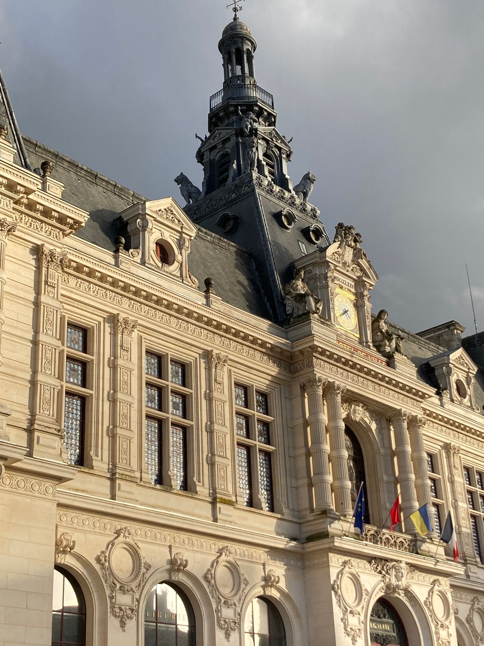 Façade et campanile de l'hôtel de ville de Poitiers avec drapeaux sous un ciel d'orage
