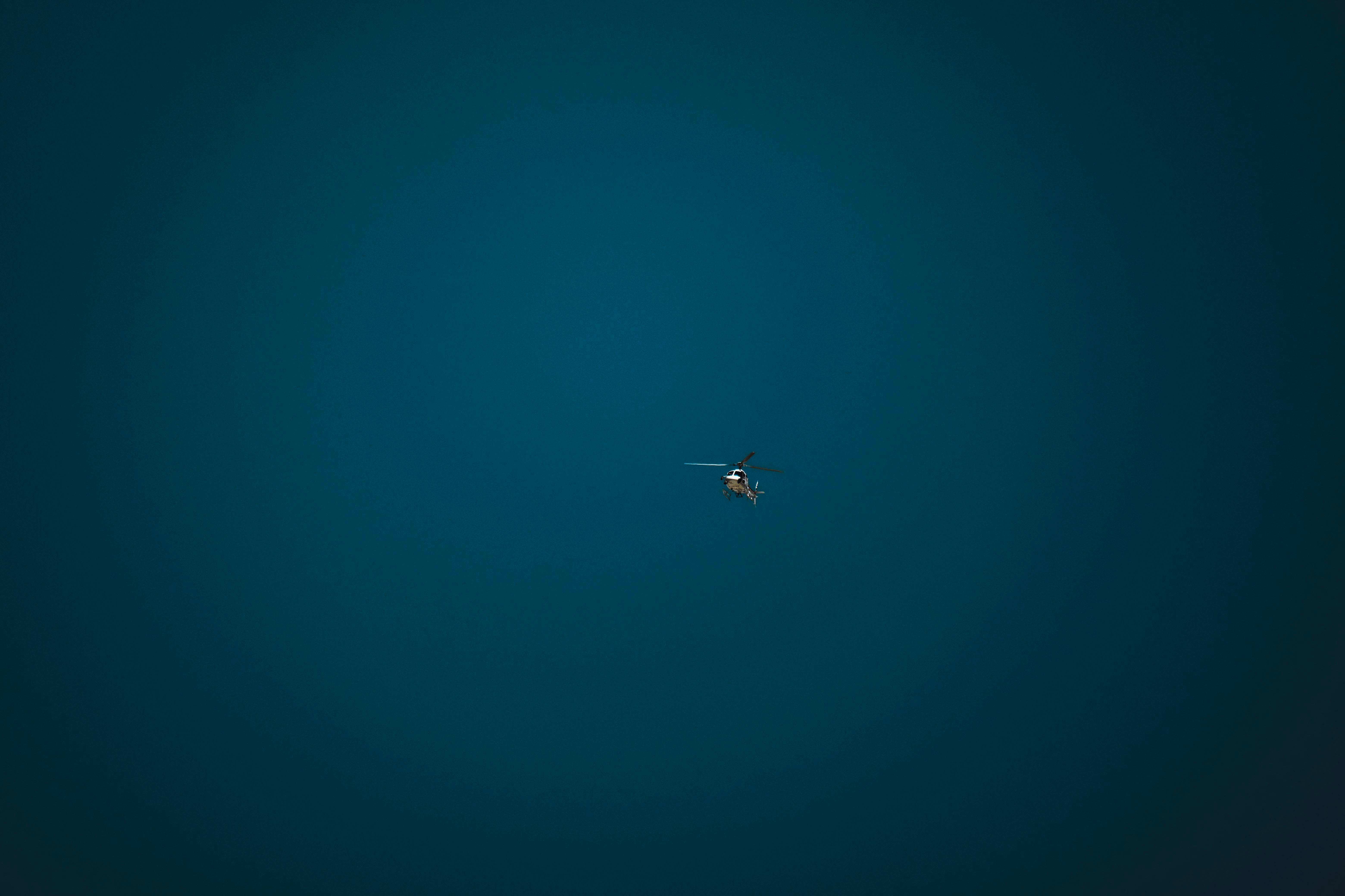 Free A small helicopter hovers alone in a vast, clear blue sky, symbolizing freedom and isolation. Stock Photo