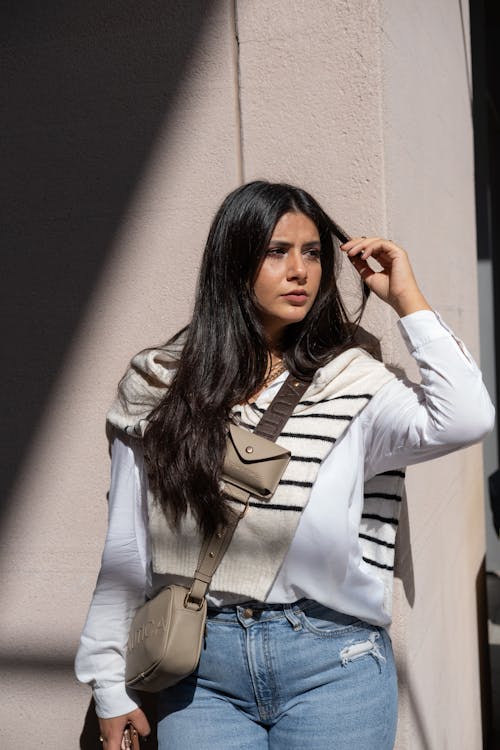 Young Woman in White Blouse and Jeans Posing by Wall