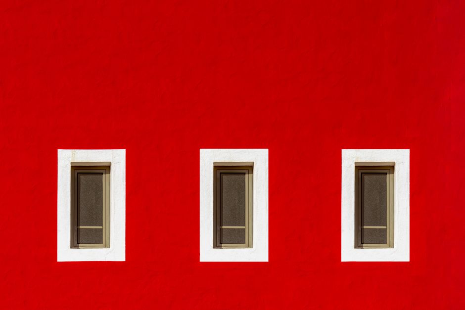 Bright red wall featuring three symmetrically arranged windows with white frames.