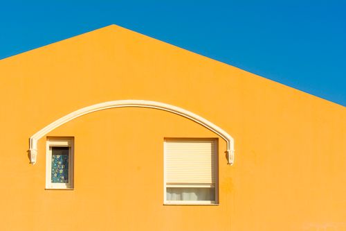 Free Bright yellow facade of a house with two windows under a clear blue sky, highlighting minimalist architecture. Stock Photo