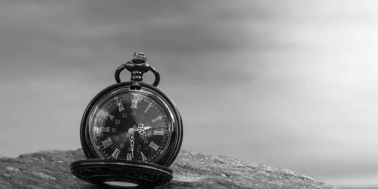 A timeless still life of a vintage pocket watch with Roman numerals on a rock in black and white.