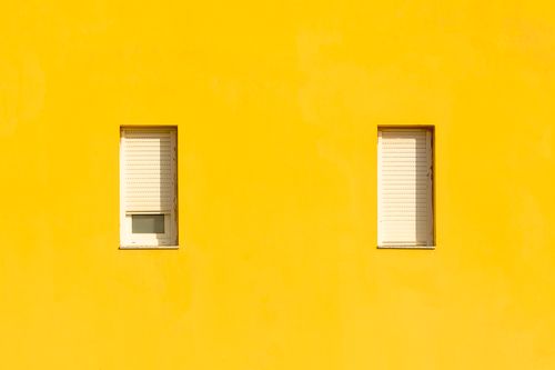 Free Bright yellow wall with two shuttered windows, creating a minimalist and modern aesthetic. Stock Photo