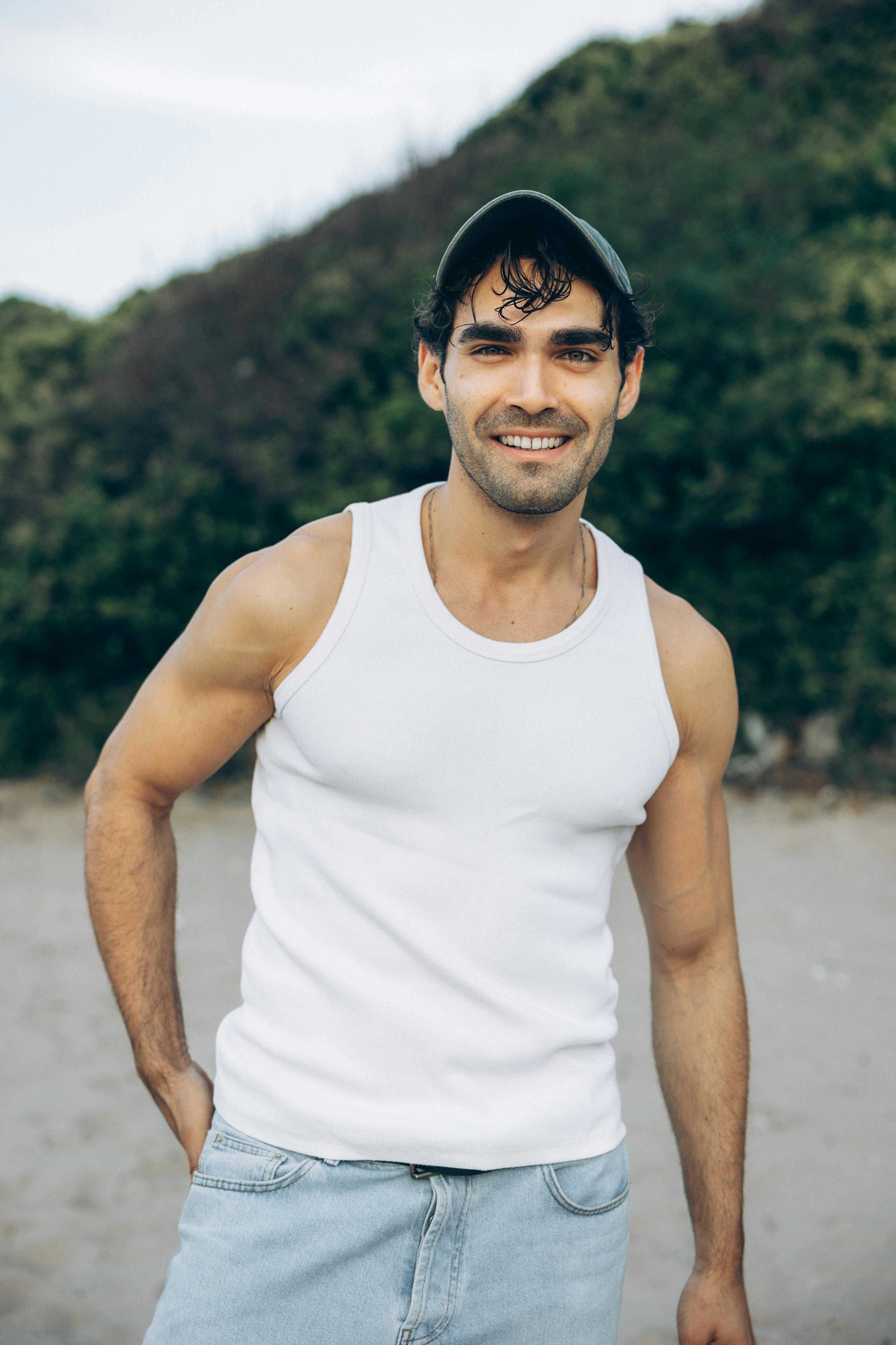 a man in a white tank top and jeans smiling