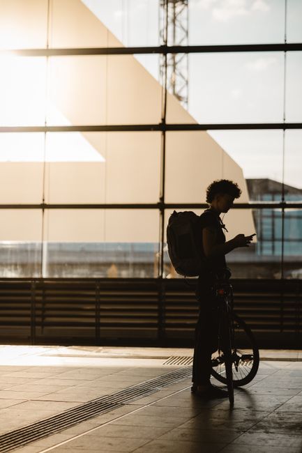 Silhouette of a man with his bicycle inside a sunlit modern Berlin urban space.