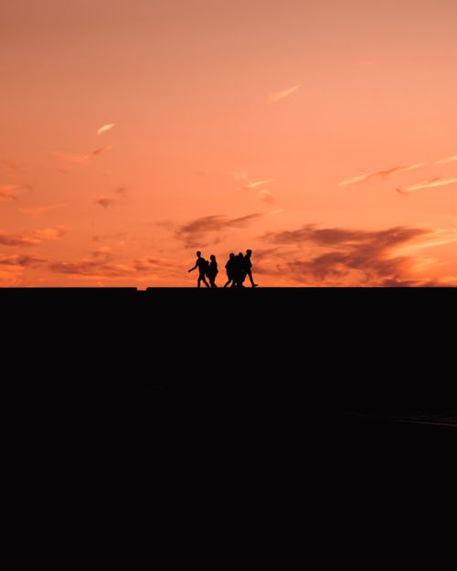 Free Silhouettes of people walking under a vivid sunset, creating a dramatic sky view. Stock Photo