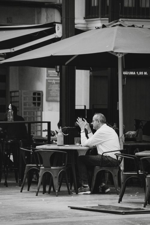 Free Elderly man sitting at an outdoor cafe table in Valencia, Spain, enjoying leisure time under an umbrella. Stock Photo