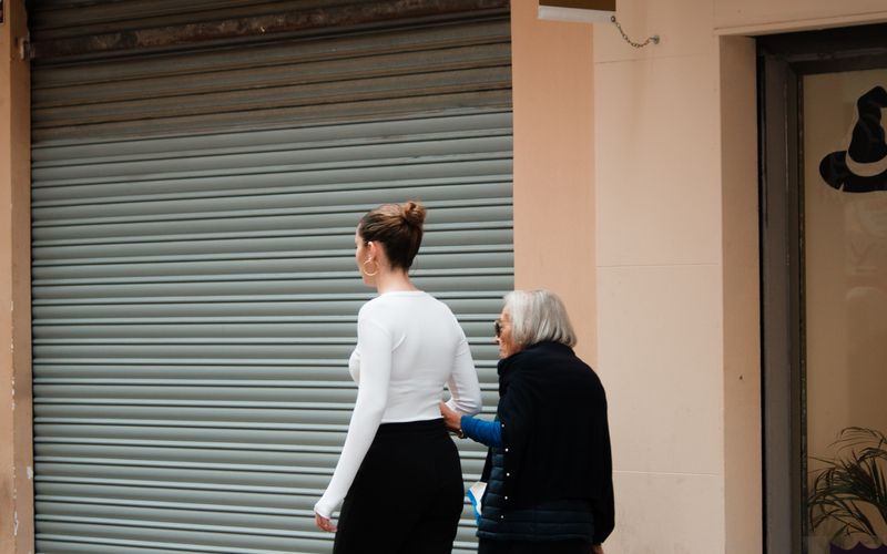 Caregiver helping elderly woman walk — mobility and movement support at home